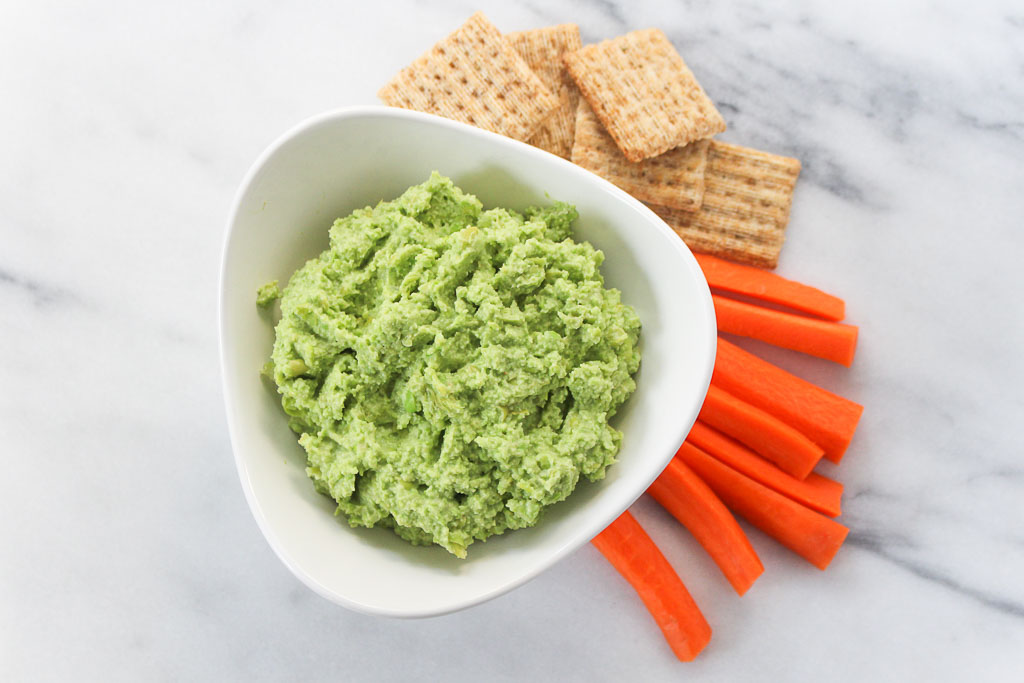 Edamame Avocado Hummus in a white bowl with carrots and crackers