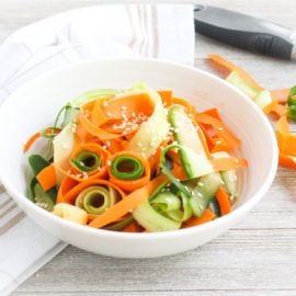 Sesame, Carrot, & Cucumber Salad in a white bowl with a vegetable peeler