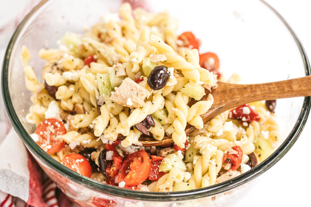 close up of Mediterranean tuna pasta salad with a scoop on a wooden spoon